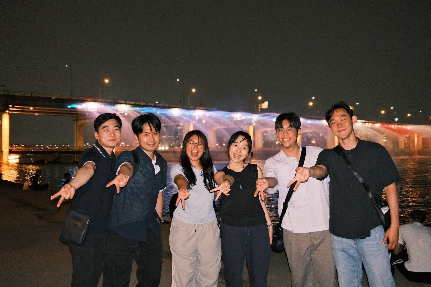 Friends posing at night by a lit-up bridge in Korea