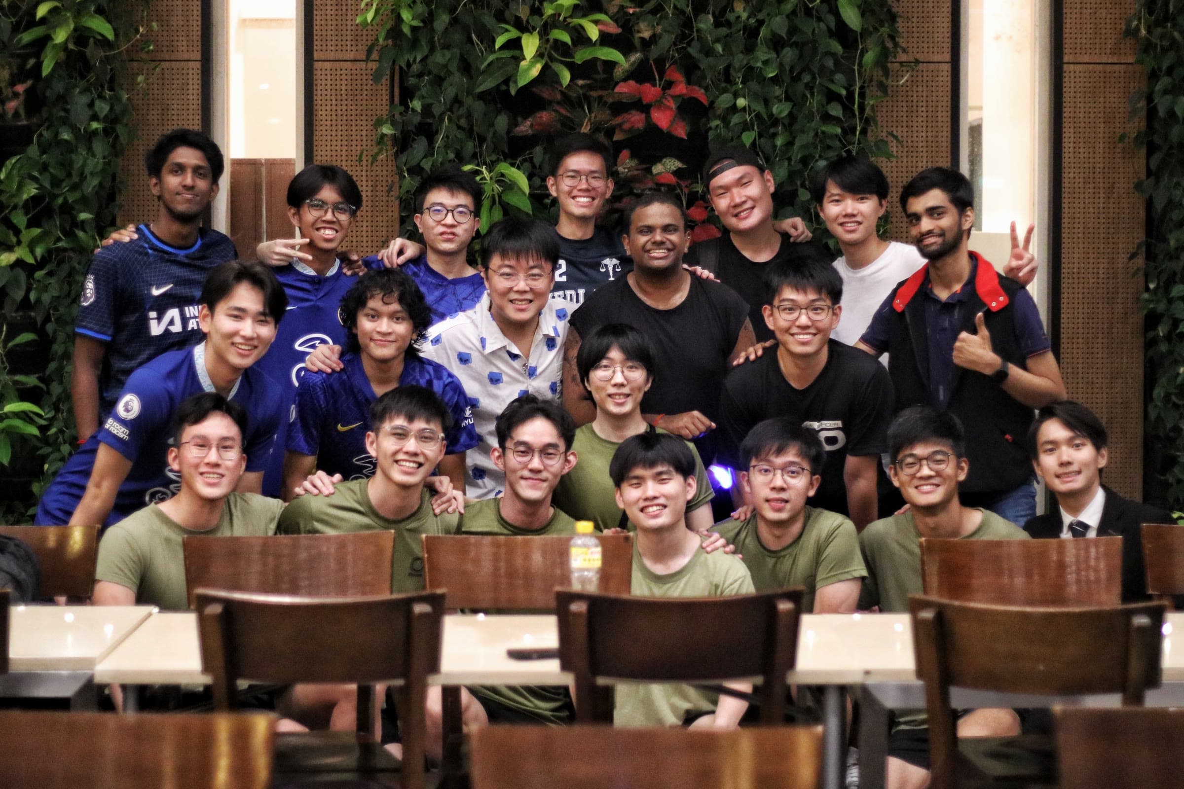 A large NUS College group in front of a green wall